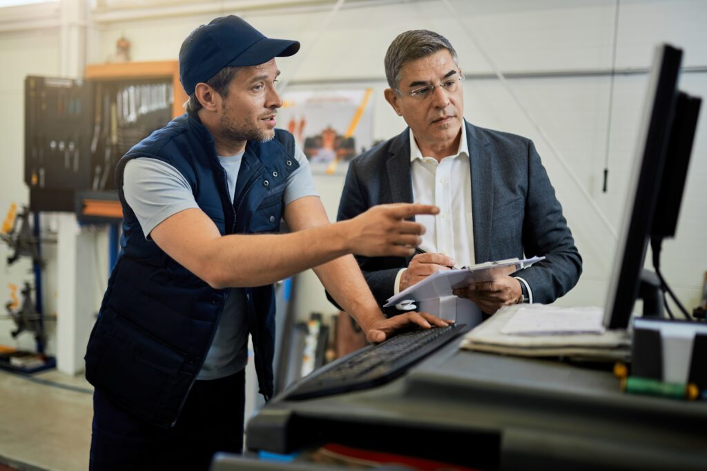 mid-adult-manager-car-mechanic-talking-while-using-computer-auto-repair-shop (1)